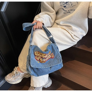 Detail of blue denim crossbody bag featuring vibrant embroidered text and wide strap
