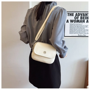 Detail of a creamy white crossbody bag with a round metal logo and textured PU leather