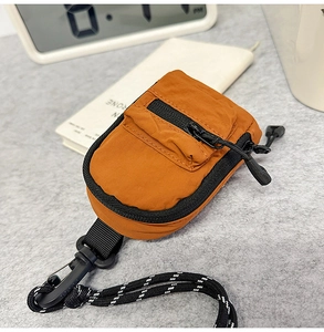 Close-up of bright orange nylon mini bag with black zipper and woven lanyard