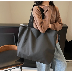 Close-up of black nylon tote bag with embossed lettering and wide shoulder straps