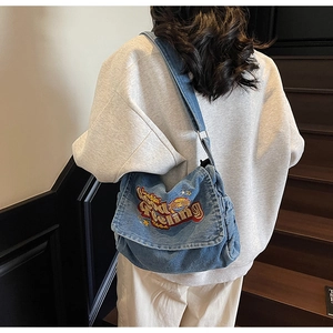 Detail of adjustable denim shoulder strap and retro embroidery on light blue crossbody bag
