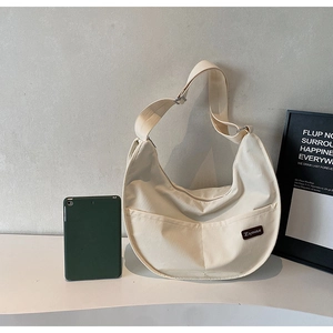 Detail view of cream canvas crescent bag showing side pockets and large capacity with a tablet