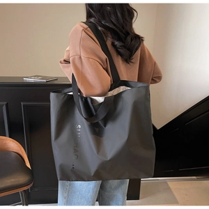 Fashionable black large capacity tote bag shown on shoulder in a modern indoor setting