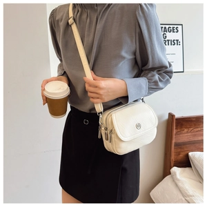 Detail of cream white small crossbody bag showing multiple compartments and metal logo