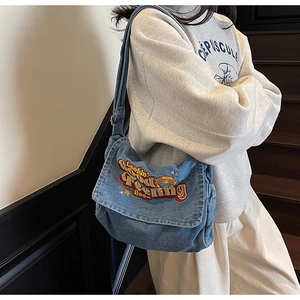 Detailed view of blue denim shoulder bag with vibrant letter embroidery and star pattern