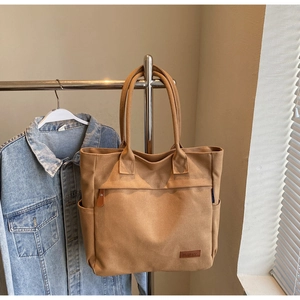 Detailed view of canvas tote bag showing front zipper pocket and leather brand logo patch