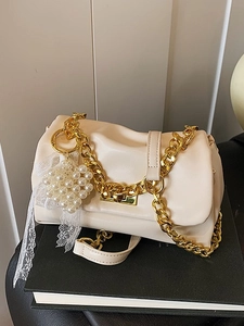 Cream-white Boston bag with gold chain, pearl heart charm and lace detail on a book