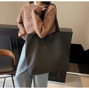 Minimalist black large capacity tote bag shown being worn by a model in a lifestyle setting