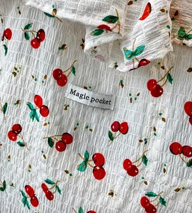 Macro view of white bubble crepe fabric with red cherry prints and woven brand label