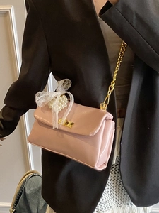 Pink faux leather shoulder bag with lace bow and pearl charm on a model's black suit
