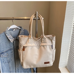 Detail of beige canvas tote bag showing side pocket and blue brand tag in soft light