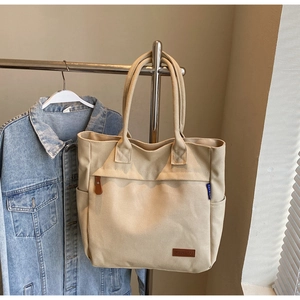 Close-up of beige canvas tote bag detailing reinforced handles and leather brand patch