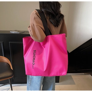 Detail view of large magenta tote bag with wide black shoulder strap and side lettering