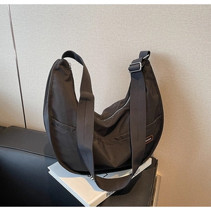 Close-up of black nylon crescent shoulder bag on a book with adjustable strap and metal buckle