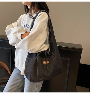 Detail of dark blue denim tote bag featuring side drawstrings and brown leather brand label