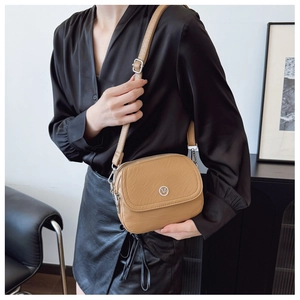 Model wearing a khaki leather crossbody bag with multiple zippers and round metal logo