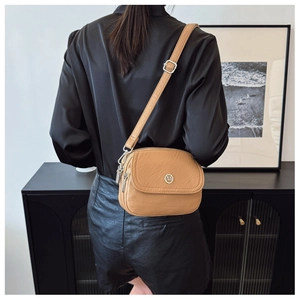 Detail of the textured camel crossbody bag with round metal logo and silver hardware