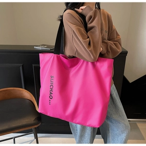 Close-up of bright fuchsia nylon tote bag with black letter print and wide shoulder strap