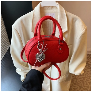Détail du sac Boston rouge avec texture grainée et pendentif en forme de cœur argenté