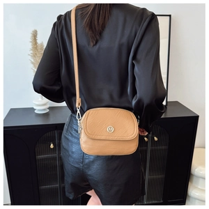 Detail of camel leather crossbody bag featuring silver round logo and pebble texture