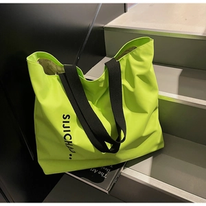 Detail view of large neon green tote bag with letter print and black fabric straps