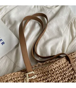Detail of woven straw tote bag featuring smooth brown leather strap and tassel accents