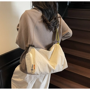 Detail of cream nylon crossbody bag featuring side zipper pocket and bright yellow strap