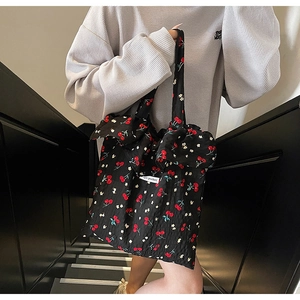 Detail of cherry print tote bag featuring textured pleated fabric and large bow on handle