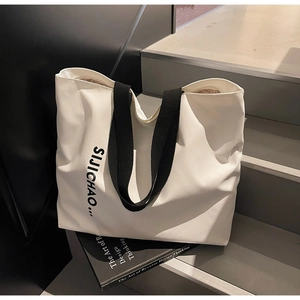 Detail of white canvas tote bag with black letter print and wide strap handles