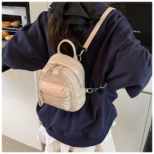 Detailed view of heart quilted cream PU leather backpack worn by model in home setting