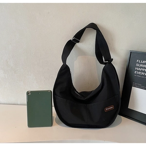 Detail view of black nylon crescent tote bag featuring a brand tag and wide adjustable strap