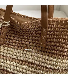 Detail of woven straw tote bag featuring brown leather handle with reinforced stitching