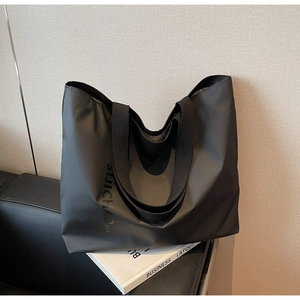 Close-up of black nylon tote bag with matte letter print on a stylish leather sofa