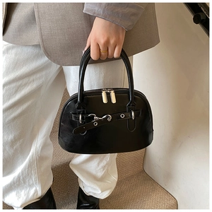 Detail of black faux leather shell bag with silver buckles and dual metal zippers