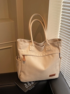 Large beige canvas tote bag with side pockets on a black sofa for daily commuting