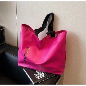 Detail view of the bright pink tote bag featuring a gold letter print and black wide straps