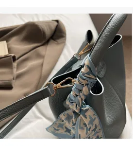 Détail du sac seau en cuir grainé bleu avec foulard en soie et boucles dorées chic