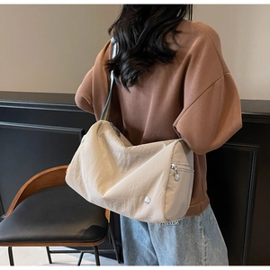 Detail of a beige nylon crossbody bag with wide striped strap and metal zipper