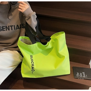 Detail of neon green nylon tote bag with black letter print and wide shoulder strap