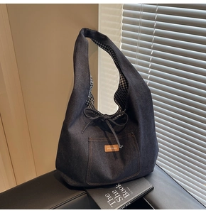 Detail of blue denim tote bag with brown leather brand label and drawstring bow detail
