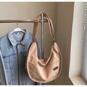 Detail of khaki nylon crescent bag featuring a brand leather patch and adjustable strap