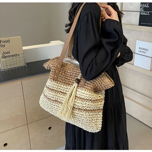 Detail of two-tone woven straw tote bag featuring brown leather strap and tassel charm
