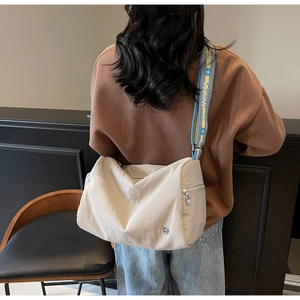 Detail of beige crossbody bag featuring adjustable blue and yellow wide logo shoulder strap