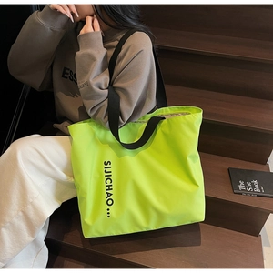 Neon green large capacity tote bag with black letter print on dark wooden stairs