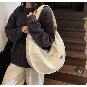 Detail of off-white crescent nylon tote bag featuring dual front pockets and logo tag