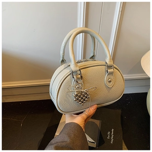 Détail du sac Boston en cuir gris clair avec breloque cœur en perles et nœud argenté