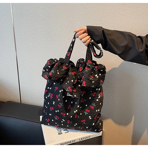 Detail of black tote bag with cherry print and decorative ruffle edge on textured fabric