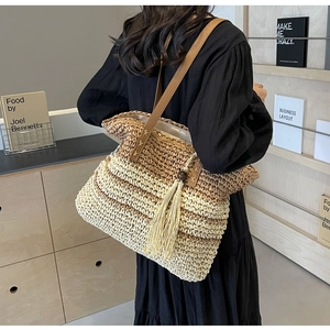 Detailed view of woven straw tote bag featuring tassel charm and leather shoulder straps