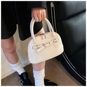 Close-up of cream-white shell handbag with decorative belt and dual metal zippers