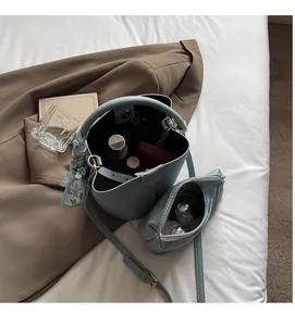 Détail du sac seau bleu clair en cuir grainé avec foulard sur une literie blanche